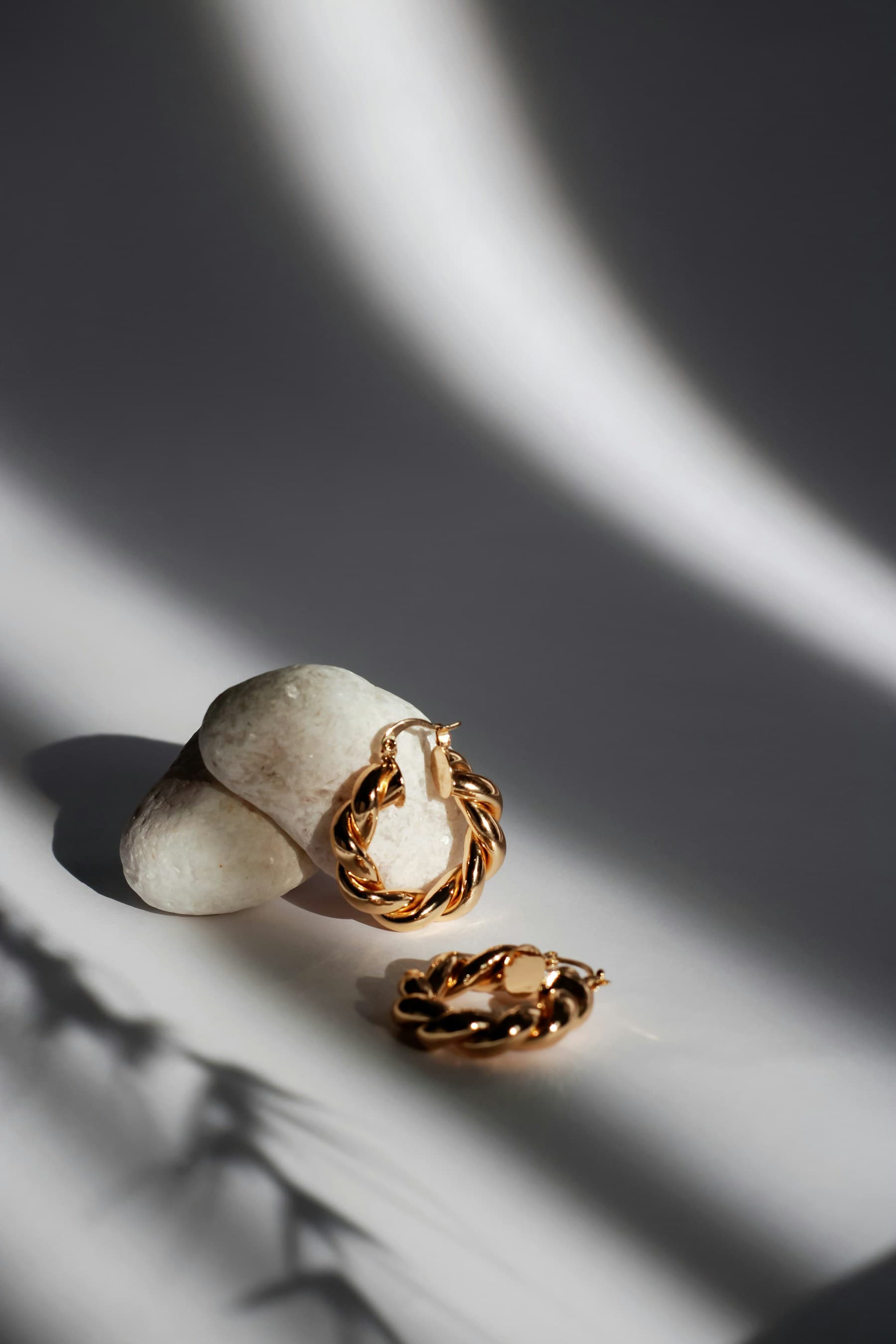 Twisted gold hoop earrings arranged on pale stones