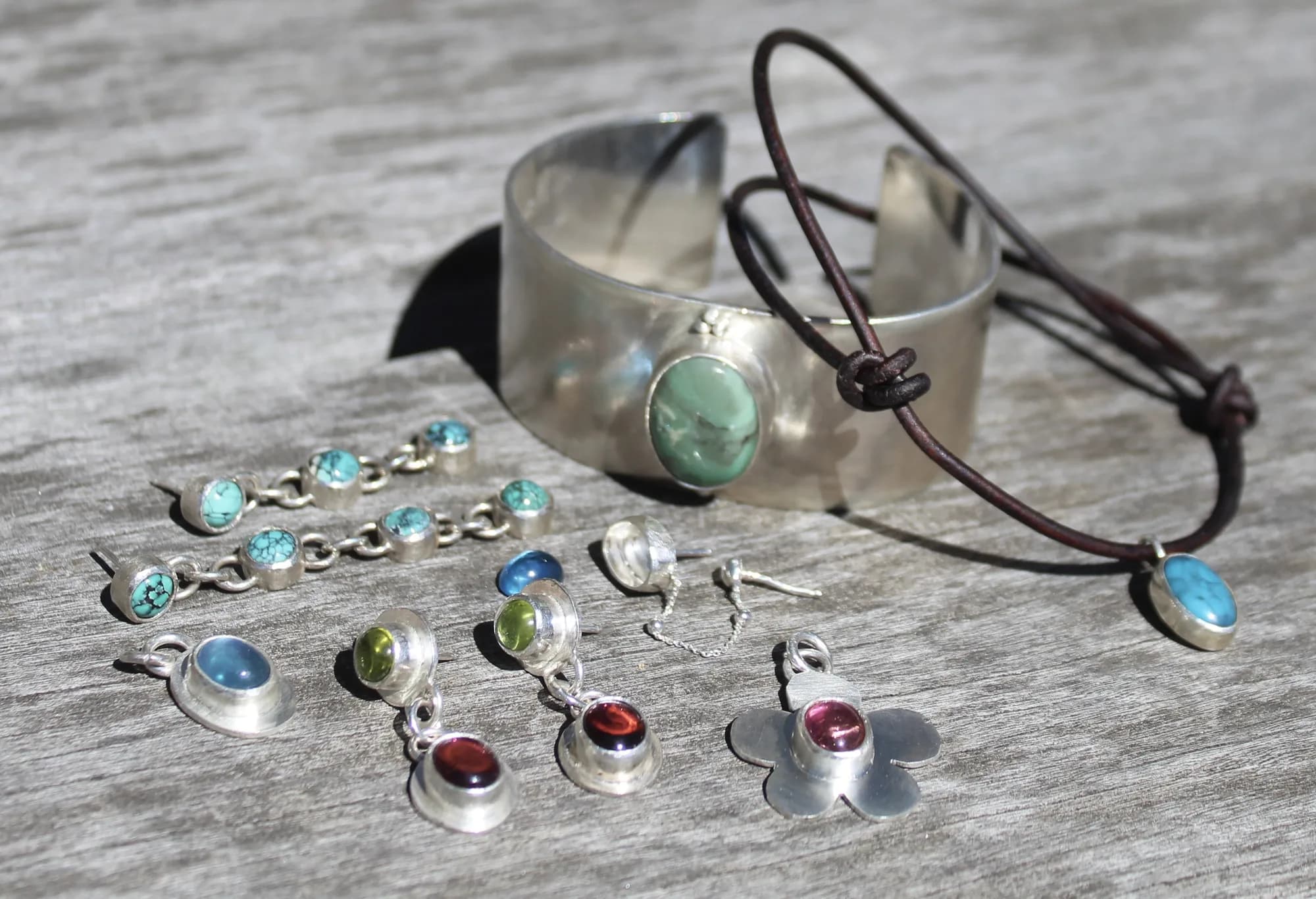 A sculptural silver cuff and colorful jewelry beside water